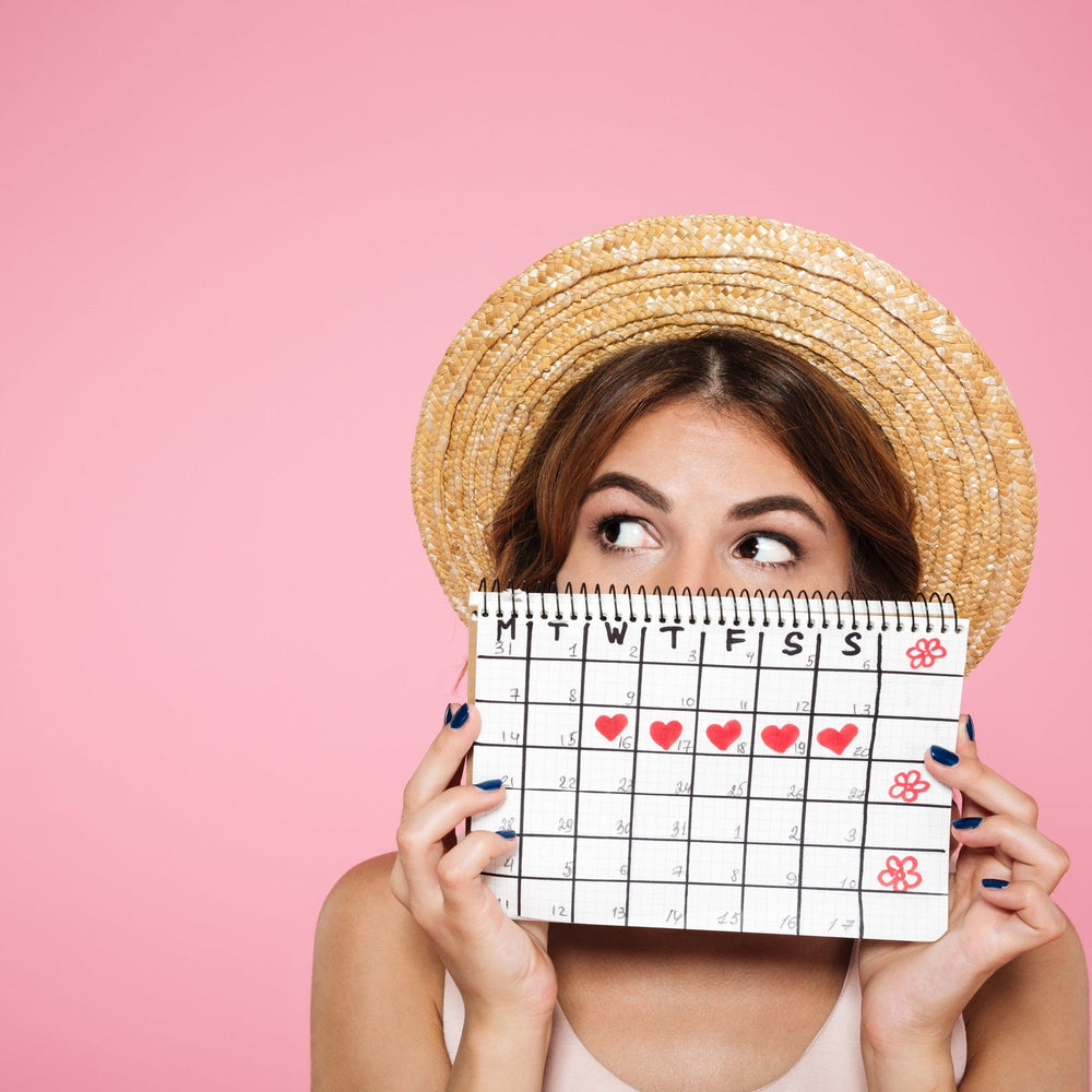 Frau mit Strohhut mit Periodenkalender in der Hand auf pinken Hintergrund 